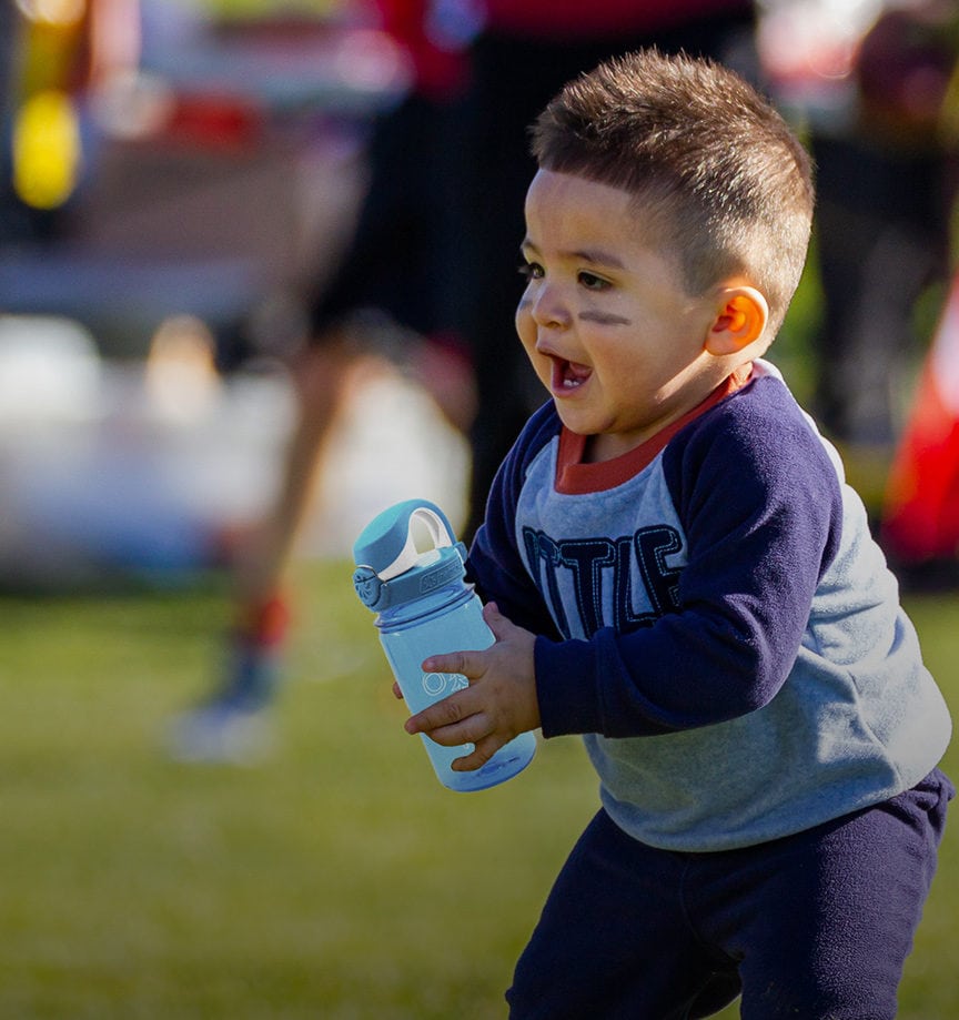 A little boy on a sports field holding a 12 oz OTF lock top bottle in blue A little boy on a sports field holding a 12 oz OTF lock top bottle in blue